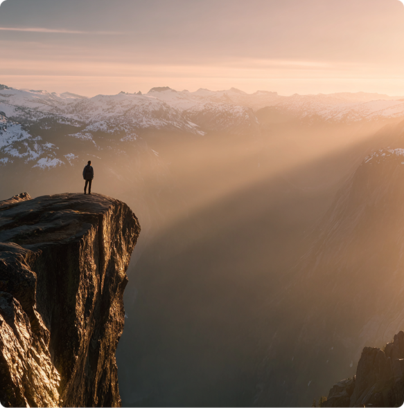 Silhouette of a traveler standing on a cliff edge at sunrise, overlooking misty mountain ranges — symbolizing exploration and reflection